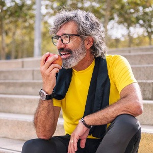 an older man enjoying an apple while sitting outside