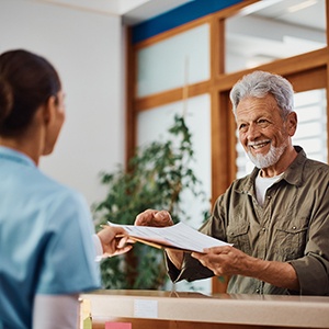 a front desk staff member handing a patient forms